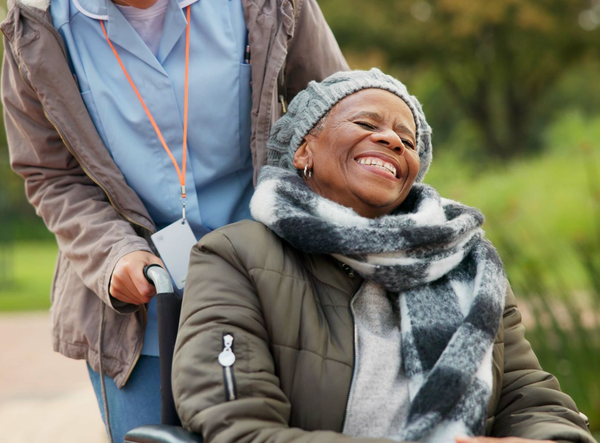 Une soignante poussant une femme âgée dans un fauteuil roulant