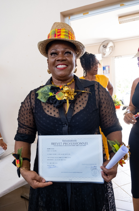 Une femme avec une robe et un chapeau aux couleurs de la Martinique, tenant un certificat professionnel