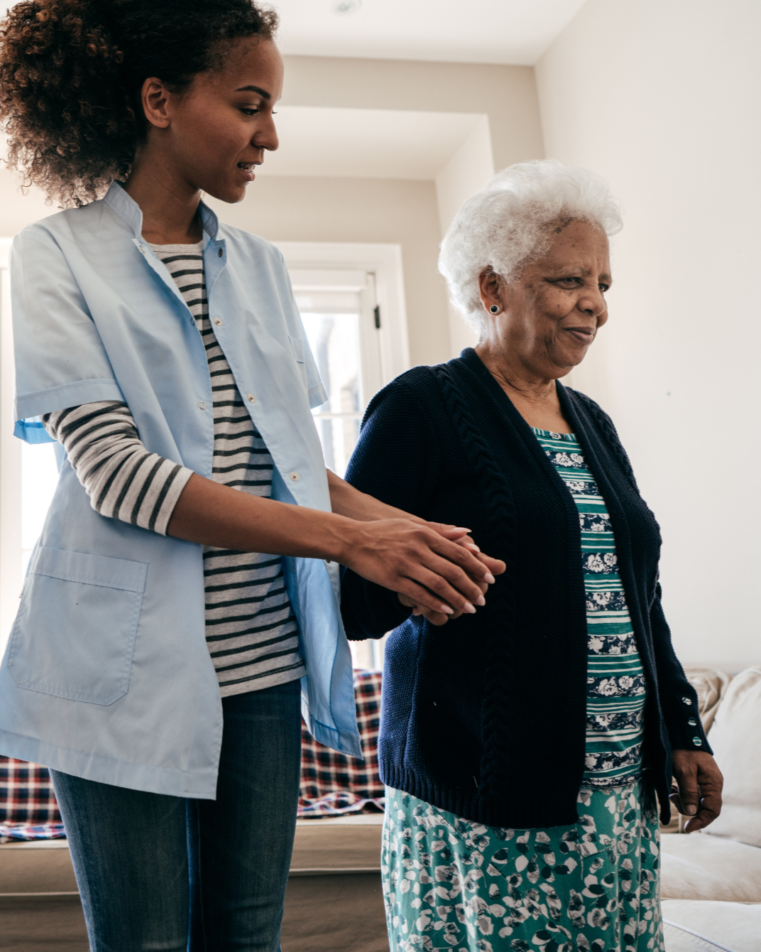 Une aide-soignante accompagne une personne âgée à l'intérieur de son domicile