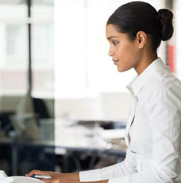Femme aux cheveux noirs en chignon portant une chemise blanche, travaillant sur un ordinateur dans un bureau
