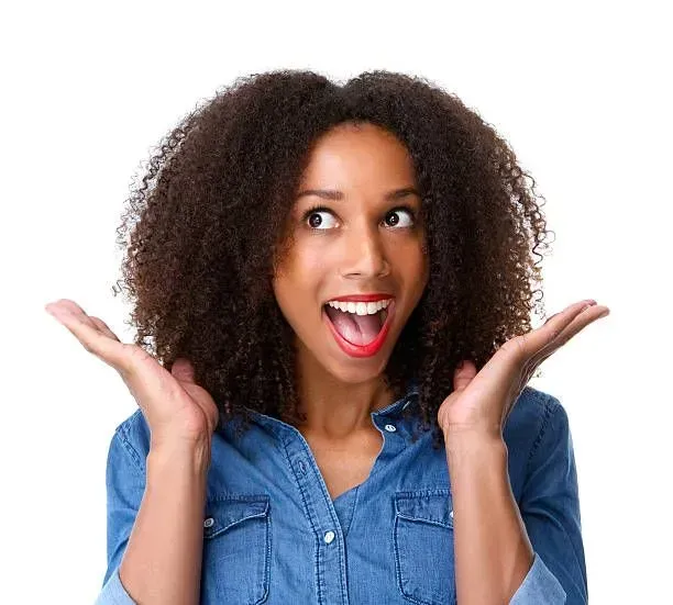 Femme aux cheveux noirs et bouclés, bouche ouverte, bras levés, l'air surpris, portant une chemise en jean