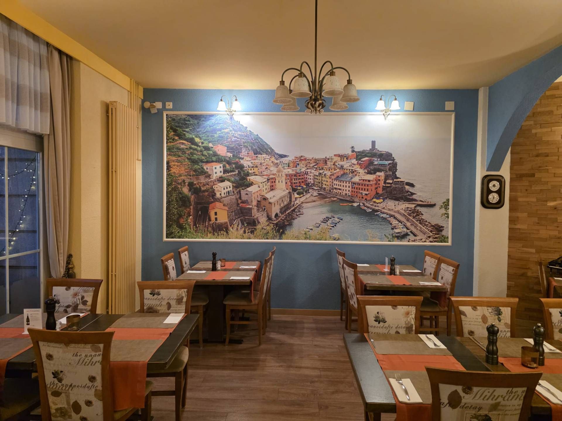 Restaurantinterieur mit Tischen und Stühlen, grosses Landschaftsfoto an blauer Wand.