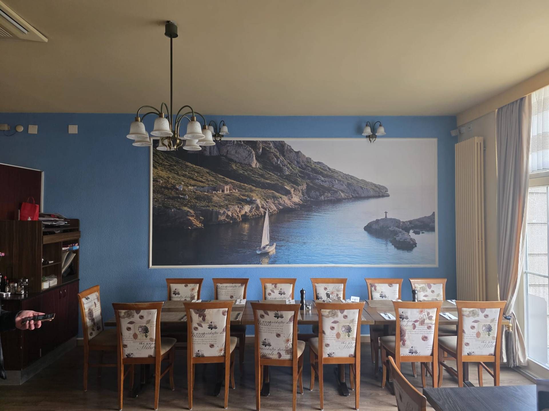 Esszimmer mit einem langen Tisch, Stühlen und einem Meeresmotiv an einer blauen Wand.