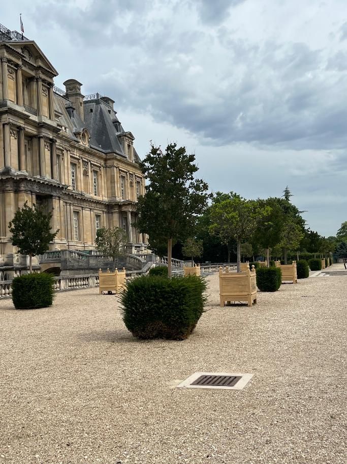 Un château en pierre avec une rangée d'arbres dans des jardinières en bois.