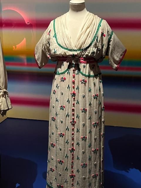 Robe sur mannequin ; lin blanc brodé de fleurs et orné de bordures vertes.