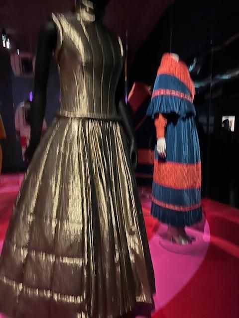 Robe dorée à jupe ample et col montant sur un mannequin, une autre robe bleue et orange.