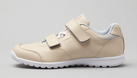 Zapatillas infantiles beige con cierre de velcro y suela blanca, vista lateral sobre fondo gris claro.