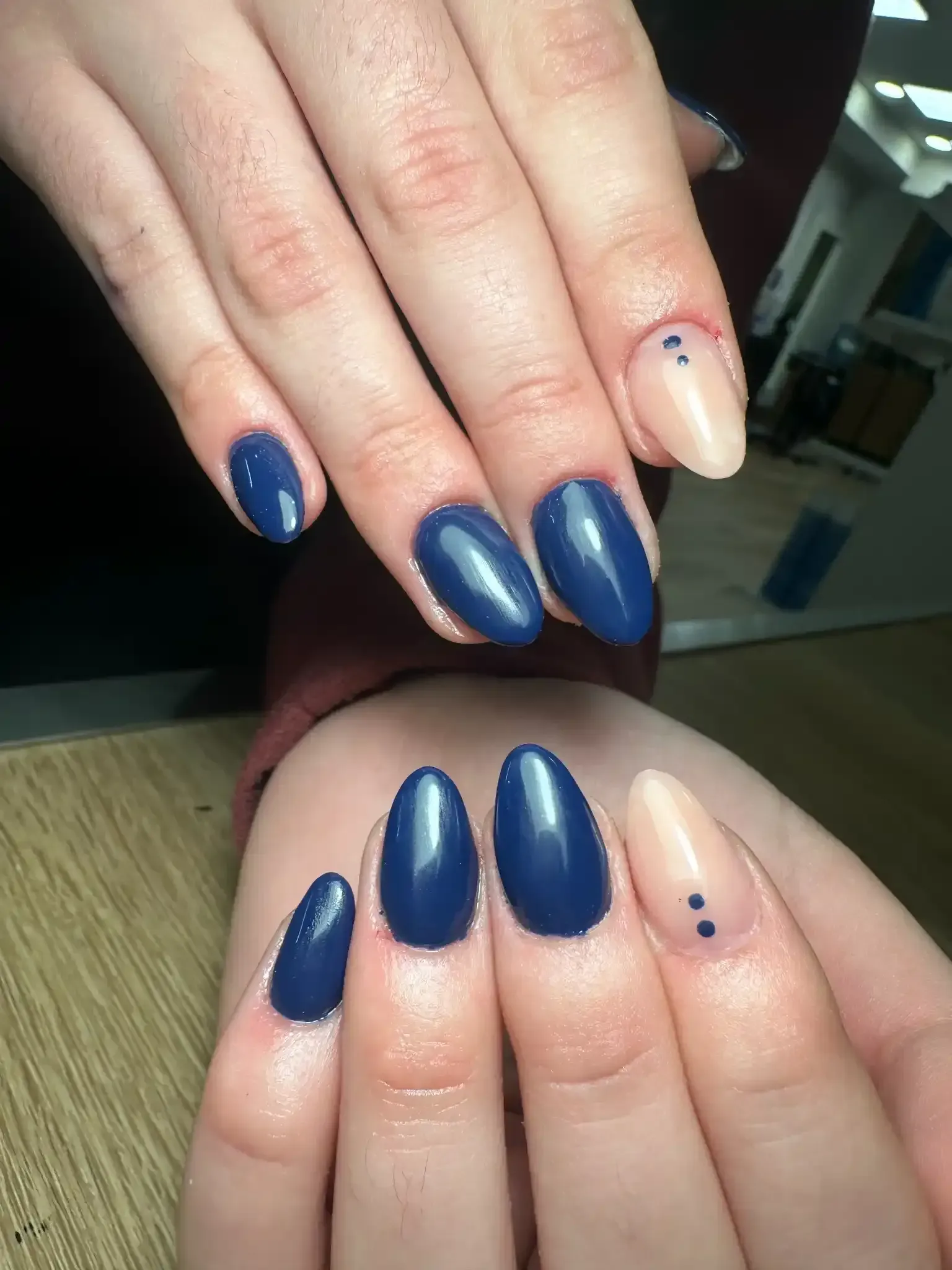 Manos con uñas en forma de almendra, algunas de color azul marino y otras de color rosa claro con puntos azul marino.