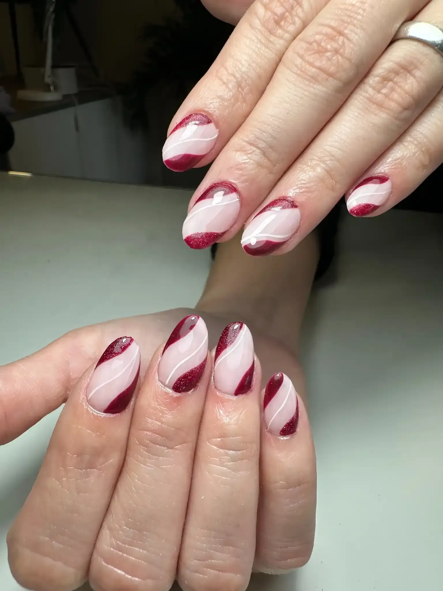 Manos con uñas en forma de almendra, diseño de remolinos en color blanco y burdeos.