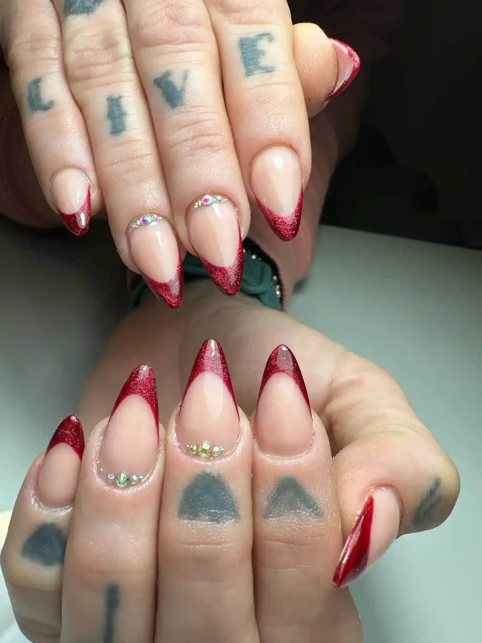 Manos con uñas largas, puntiagudas y transparentes, puntas de brillantina roja.
