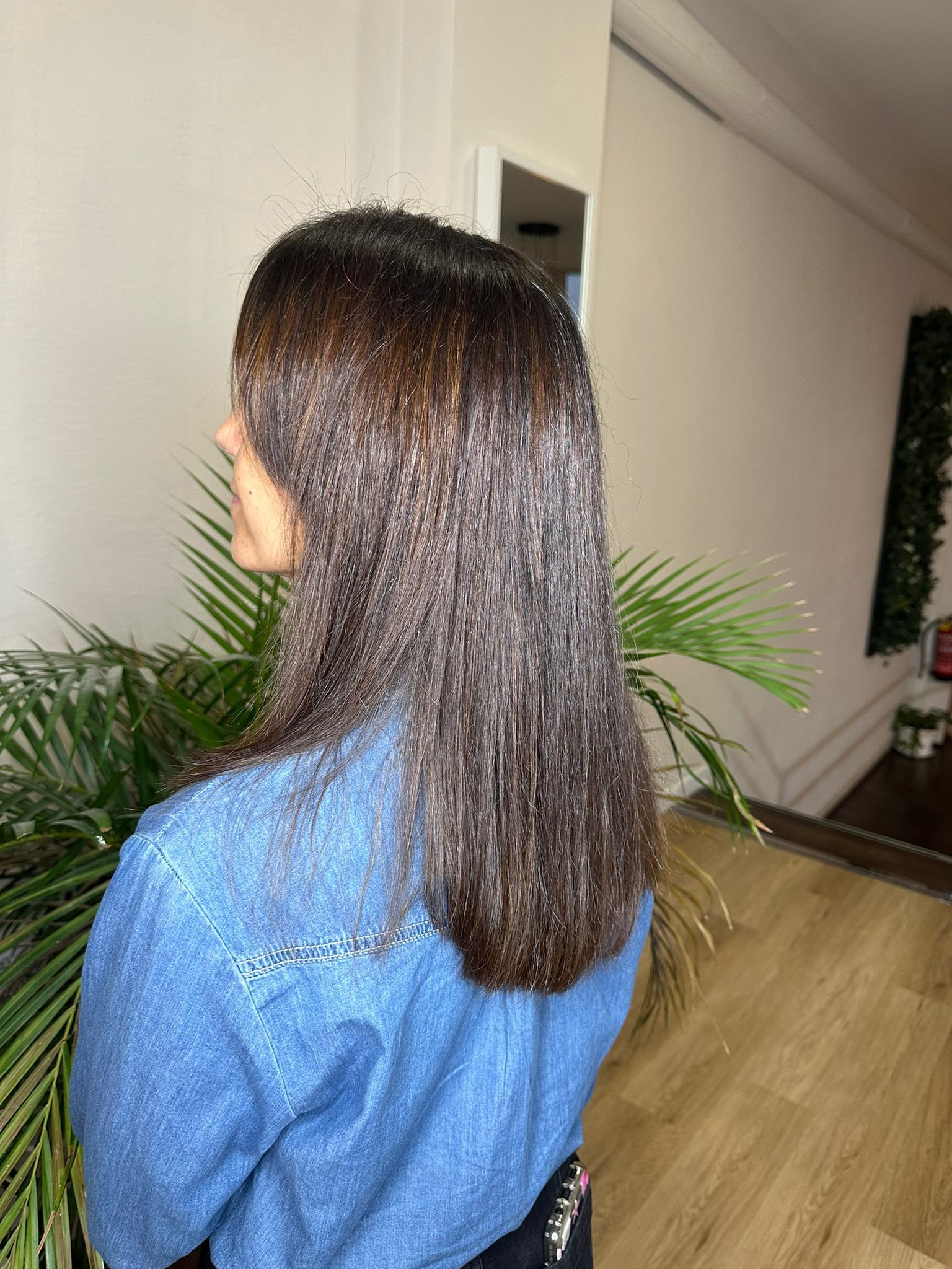 Mujer con cabello rubio largo y ondulado, vestida con una chaqueta negra, de espaldas a la cámara.