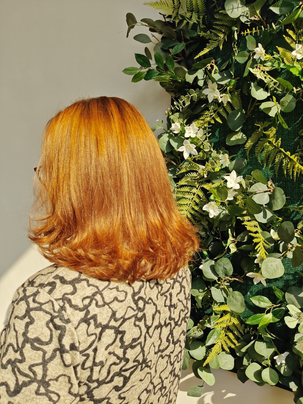 Mujer con cabello rubio largo y ondulado, vestida con una chaqueta negra, de espaldas a la cámara.