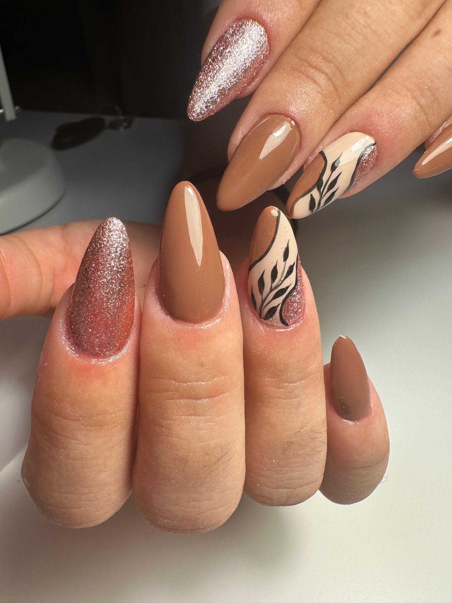 Manos con uñas en forma de almendra, algunas de color azul marino y otras de color rosa claro con puntos azul marino.