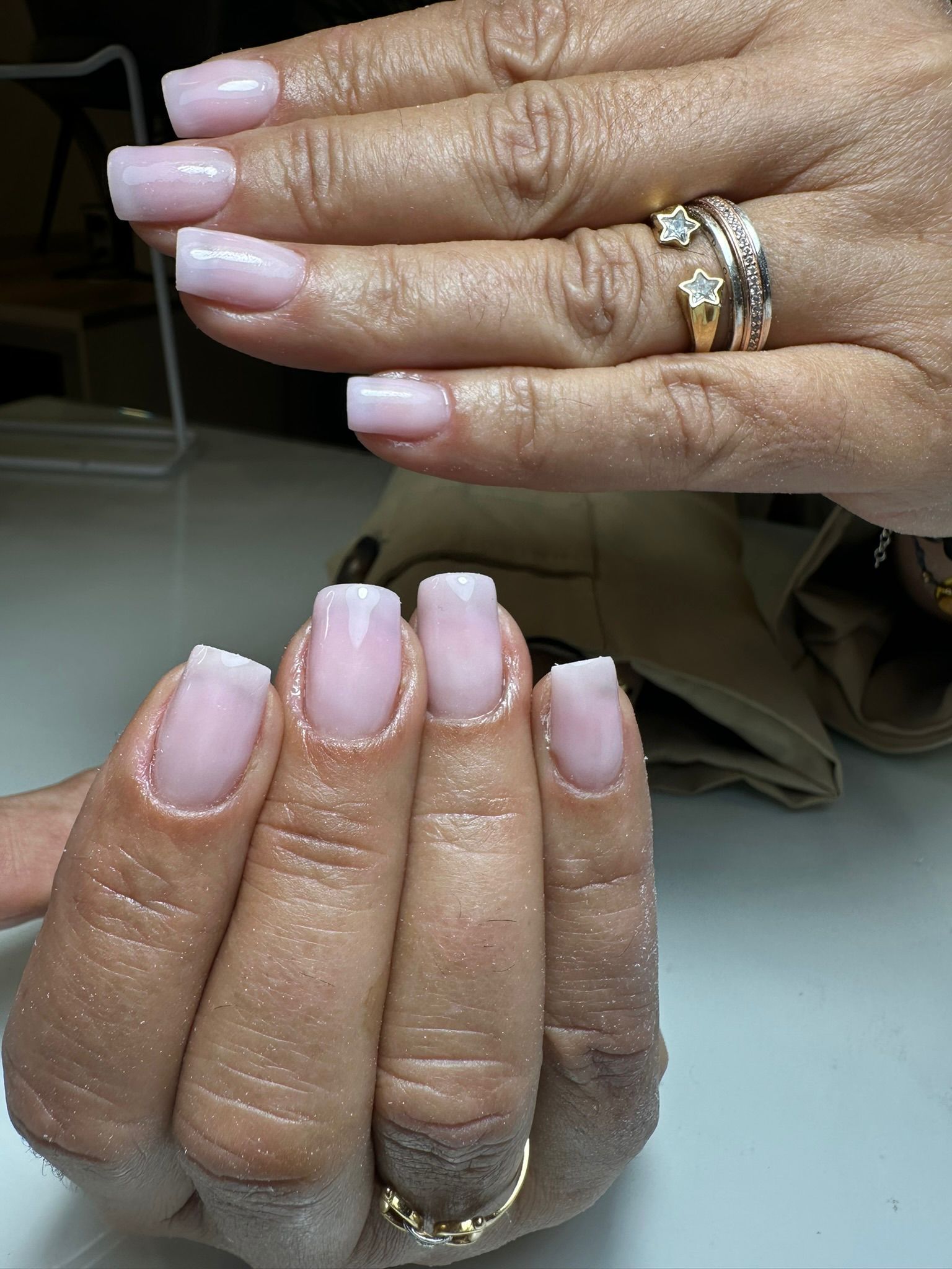 Primer plano de manos con uñas ovaladas, decoradas con purpurina rosa claro y dorada. Dos uñas tienen rayas blancas.