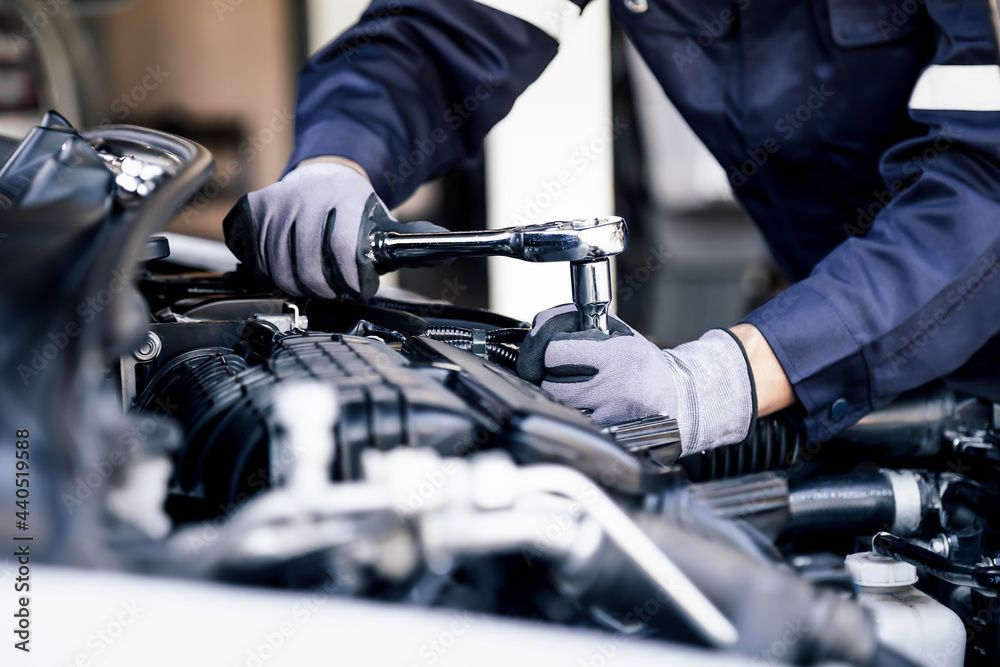 Ein Mechaniker repariert mit einem Schraubenschlüssel einen Automotor in einer Garage.