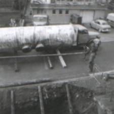 Schwarz-Weiss-Strassenszene mit einem Tankwagen, einem Soldaten und geparkten Autos in der Nähe eines Gebäudes
