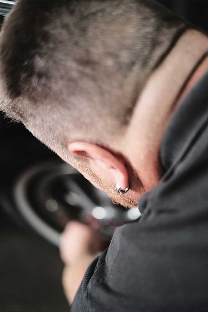 Ein Mechaniker beugt sich über ein Autorad und arbeitet in einer dunklen Garage konzentriert mit einem Werkzeug.