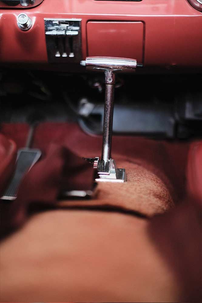 Oldtimer-Interieur mit manueller Bodenschaltung auf rotem Teppichboden.