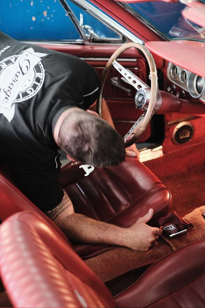 Eine Person beugt sich in den Innenraum eines roten Autos und greift nach Mittelkonsole und Sitzbereich.