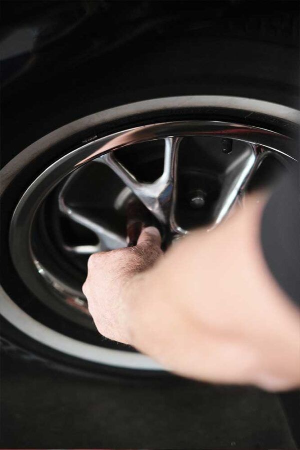 Eine Hand greift in die Felge eines Autos und zieht die Radmutter fest oder löst sie.