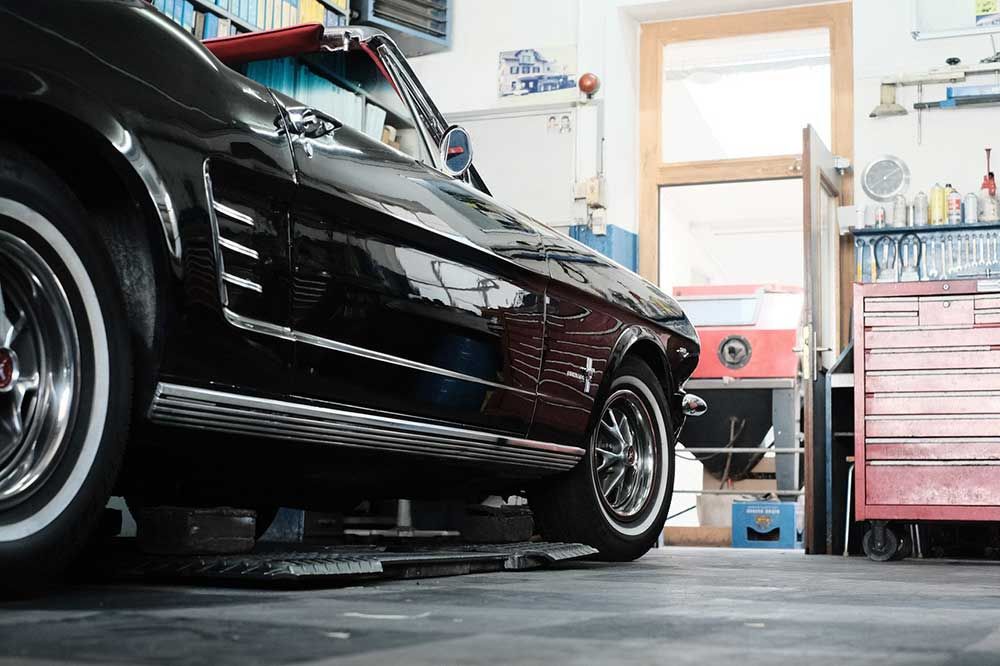 Ein schwarzer Sportwagen in einer Autowerkstatt neben Werkzeugschränken und einer Hebebühne.
