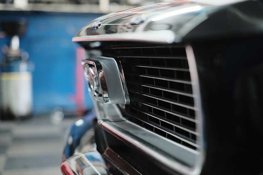 Nahaufnahme eines schwarzen Oldtimer-Kühlergrills und Chromleisten in einer Garagenumgebung