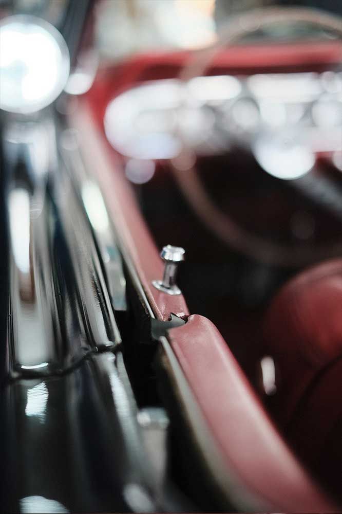 Nahaufnahme des Innenraums eines roten Autos mit verchromtem Schalthebel und verschwommenen Bedienelementen am Armaturenbrett.