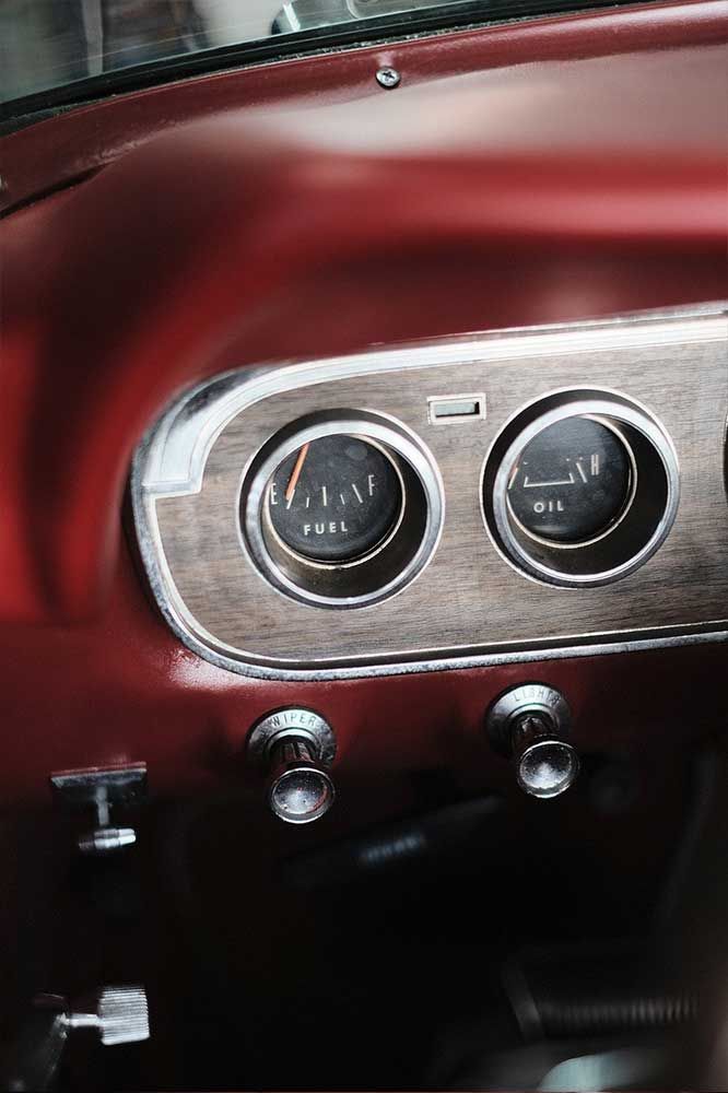 Nahaufnahme eines Oldtimer-Armaturenbretts mit zwei runden Instrumenten und verchromten Knöpfen auf einer bordeauxroten Platte