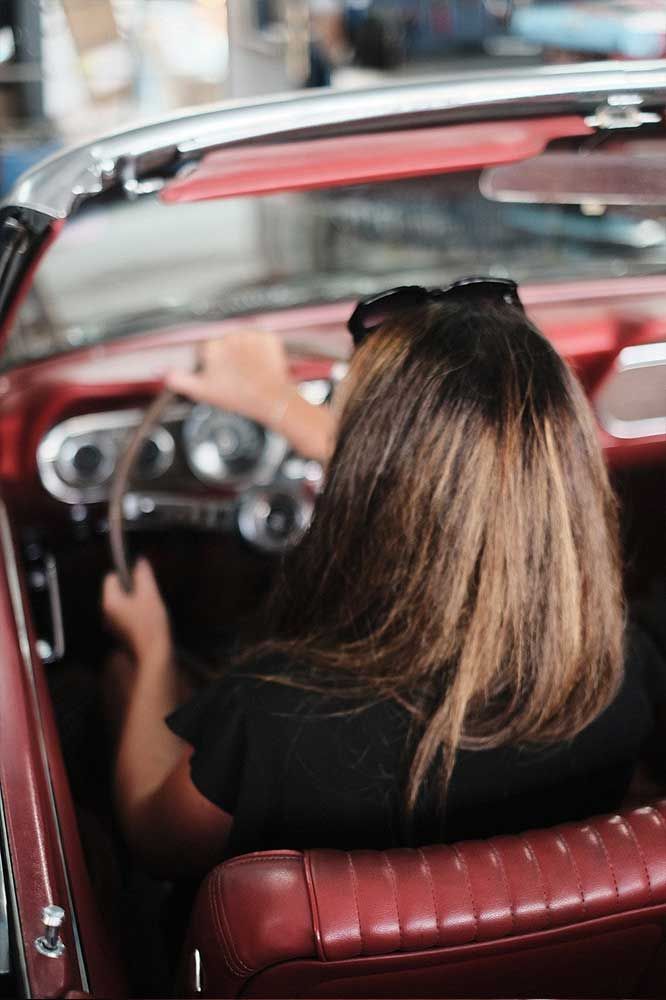 Person, die ein rotes Cabriolet mit offenem Verdeck fährt, von hinten gesehen.