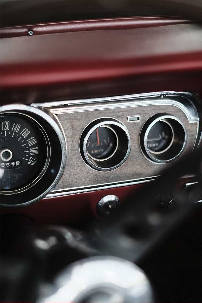 Nahaufnahme des Armaturenbretts eines Oldtimers mit verchromten Instrumenten und roter Innenausstattung.