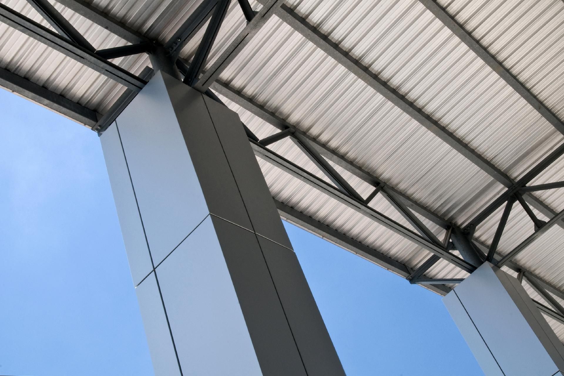 Moderne Metalldachkonstruktion mit Stützpfeilern vor blauem Himmel.