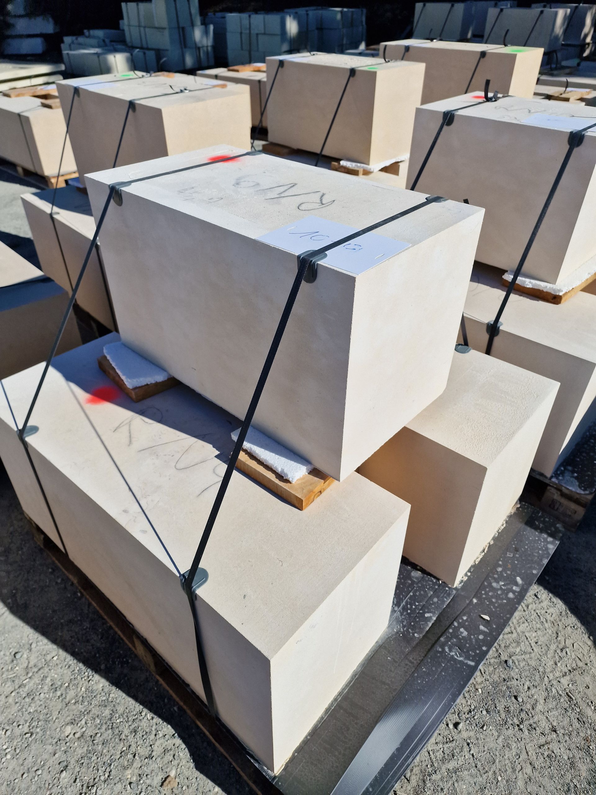 Des blocs rectangulaires en pierre claire, empilés et maintenus par des sangles en plastique noir, sont posés sur une palette en bois à l'extérieur.