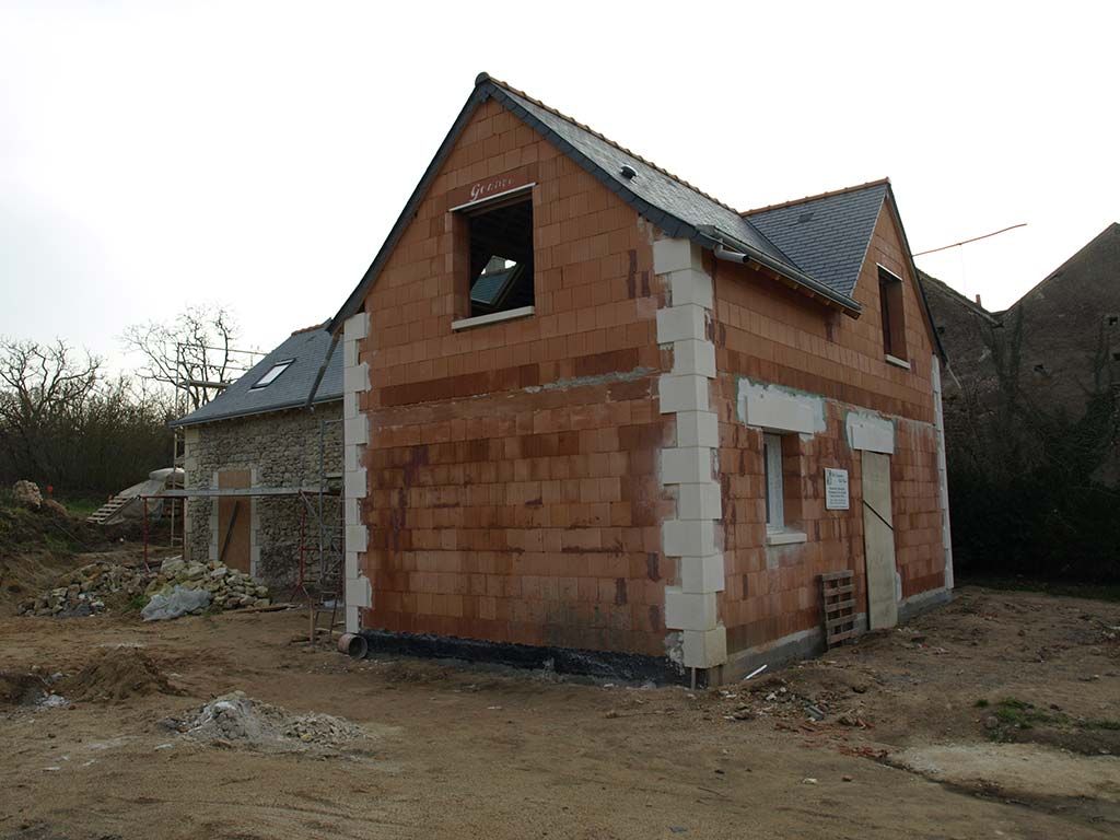 Une maison à deux étages en construction, avec des murs en briques rouges, des pierres d'angle blanches et un toit à pignon en ardoise sombre.