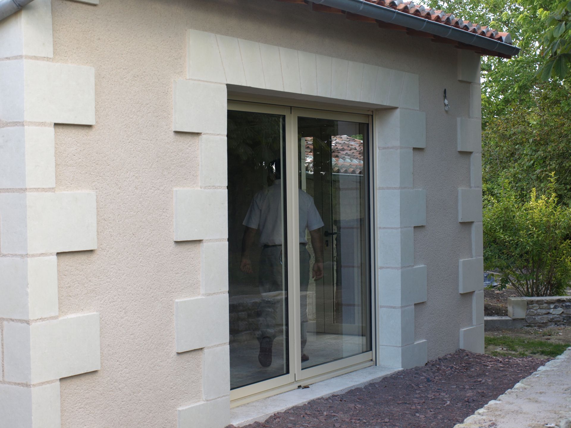 Façade beige du bâtiment avec une porte coulissante en verre encadrée de blocs de pierre décoratifs de couleur claire.