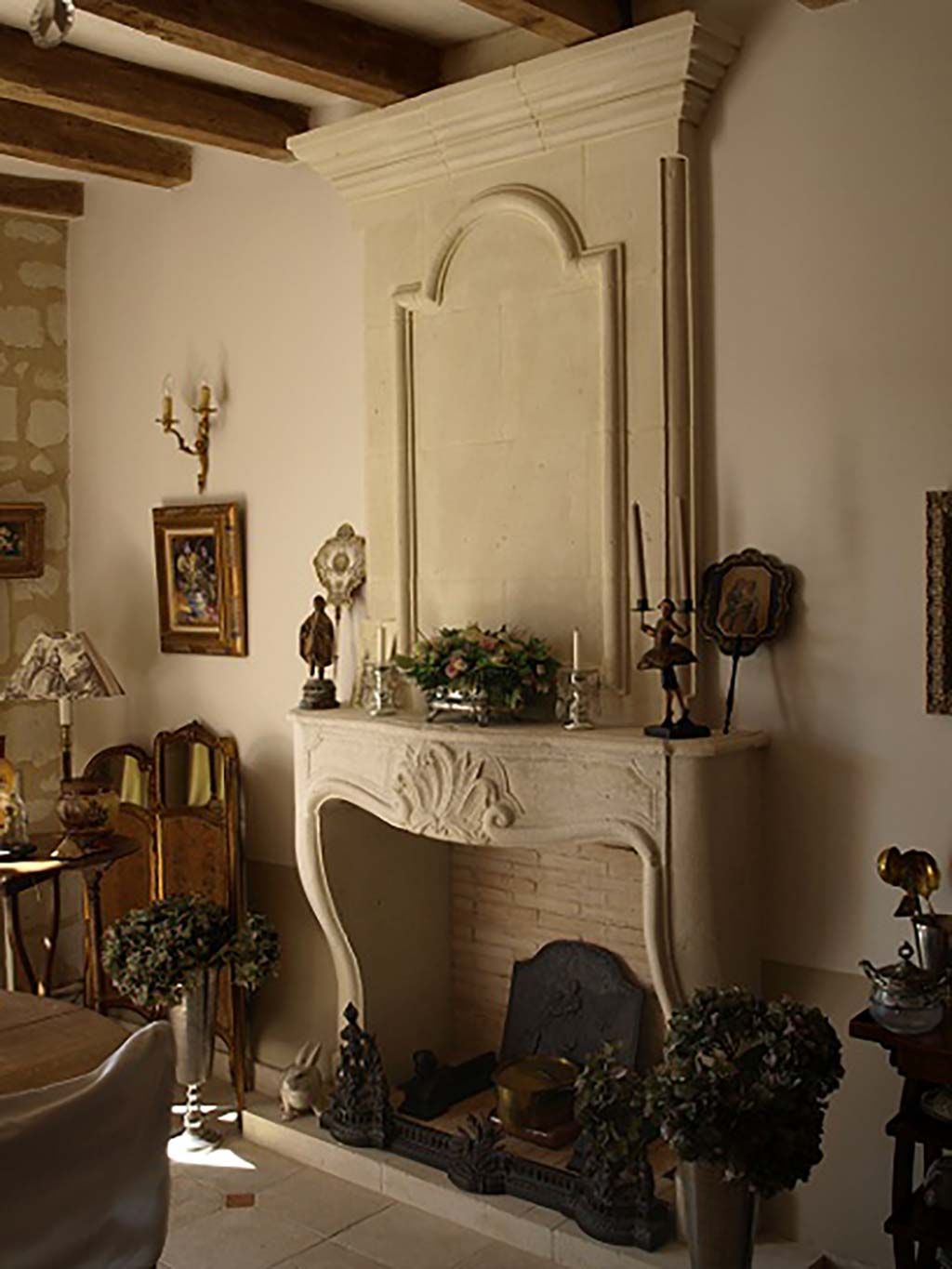 Une cheminée ornée en pierre claire, avec un manteau sculpté et un haut panneau de cheminée, dans une pièce rustique au style élégant.