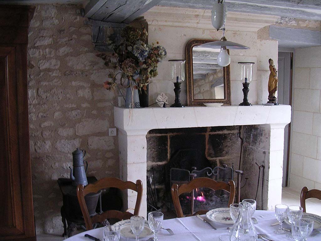 Une salle à manger rustique avec une cheminée en pierre, une table dressée pour le dîner et un mur en pierre en arrière-plan.