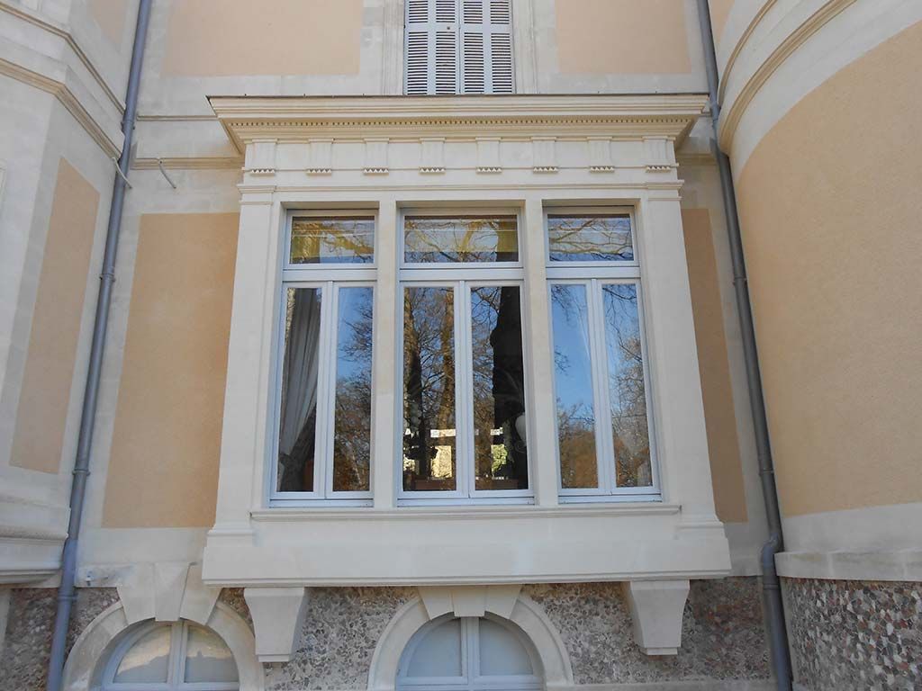 Une baie vitrée en pierre à trois carreaux sur une façade de couleur pêche, avec deux fenêtres cintrées au sous-sol.