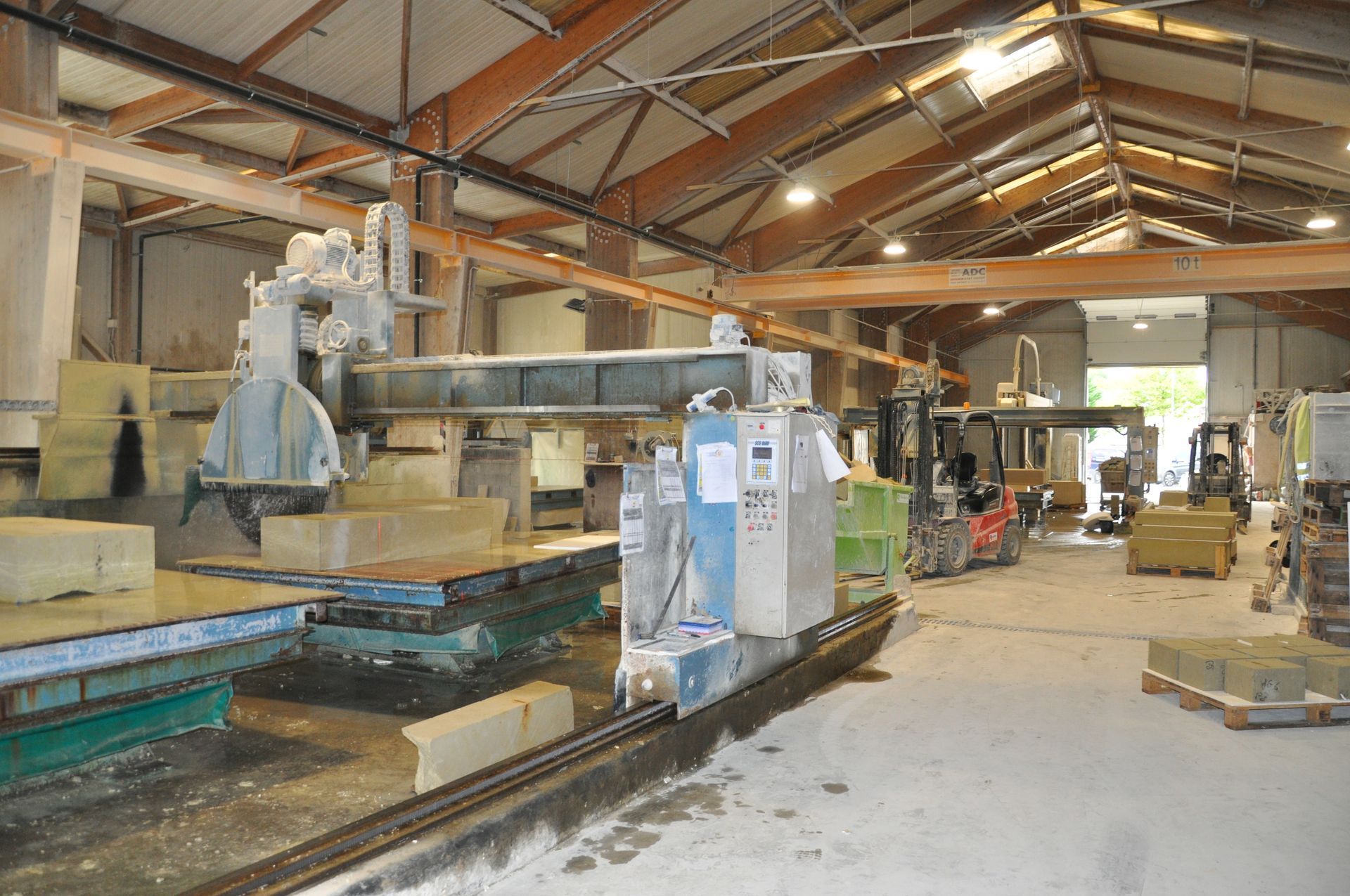 Machines industrielles de découpe de pierre avec une grande lame de scie circulaire dans un atelier spacieux avec de hautes poutres en bois.