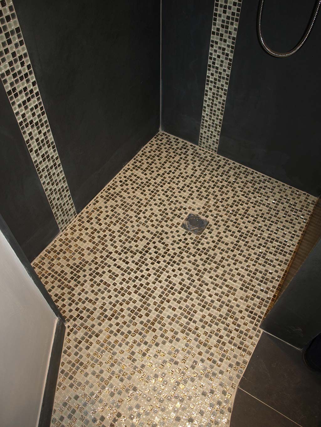 Une douche à l'italienne avec un sol en mosaïque beige et marron, des murs gris anthracite et des frises verticales en mosaïque.
