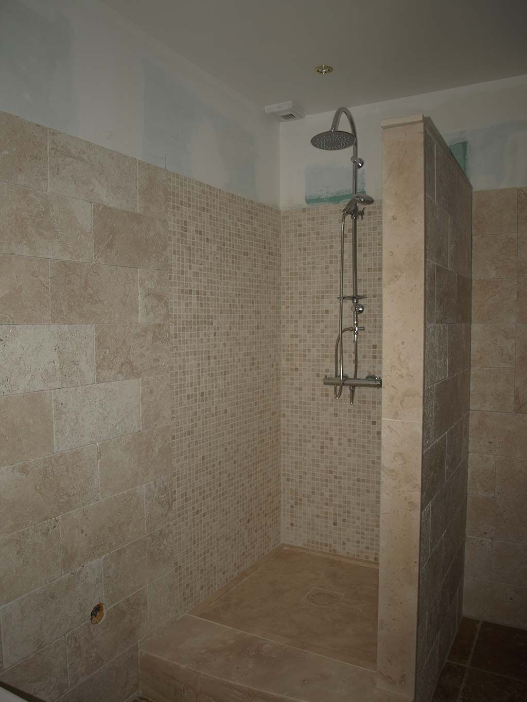 Une cabine de douche à l'italienne carrelée avec une pomme de douche en acier inoxydable fixée au mur du fond.