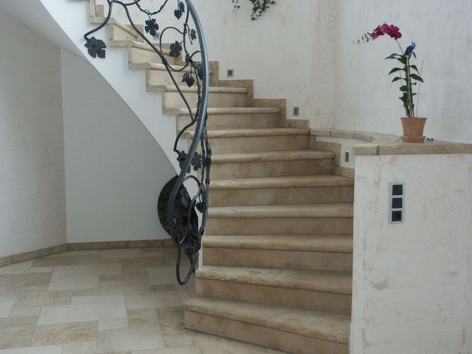 Escalier en pierre incurvé avec rampes en fer forgé ouvragées, dans un intérieur moderne et lumineux agrémenté d'un petit pot de fleurs.