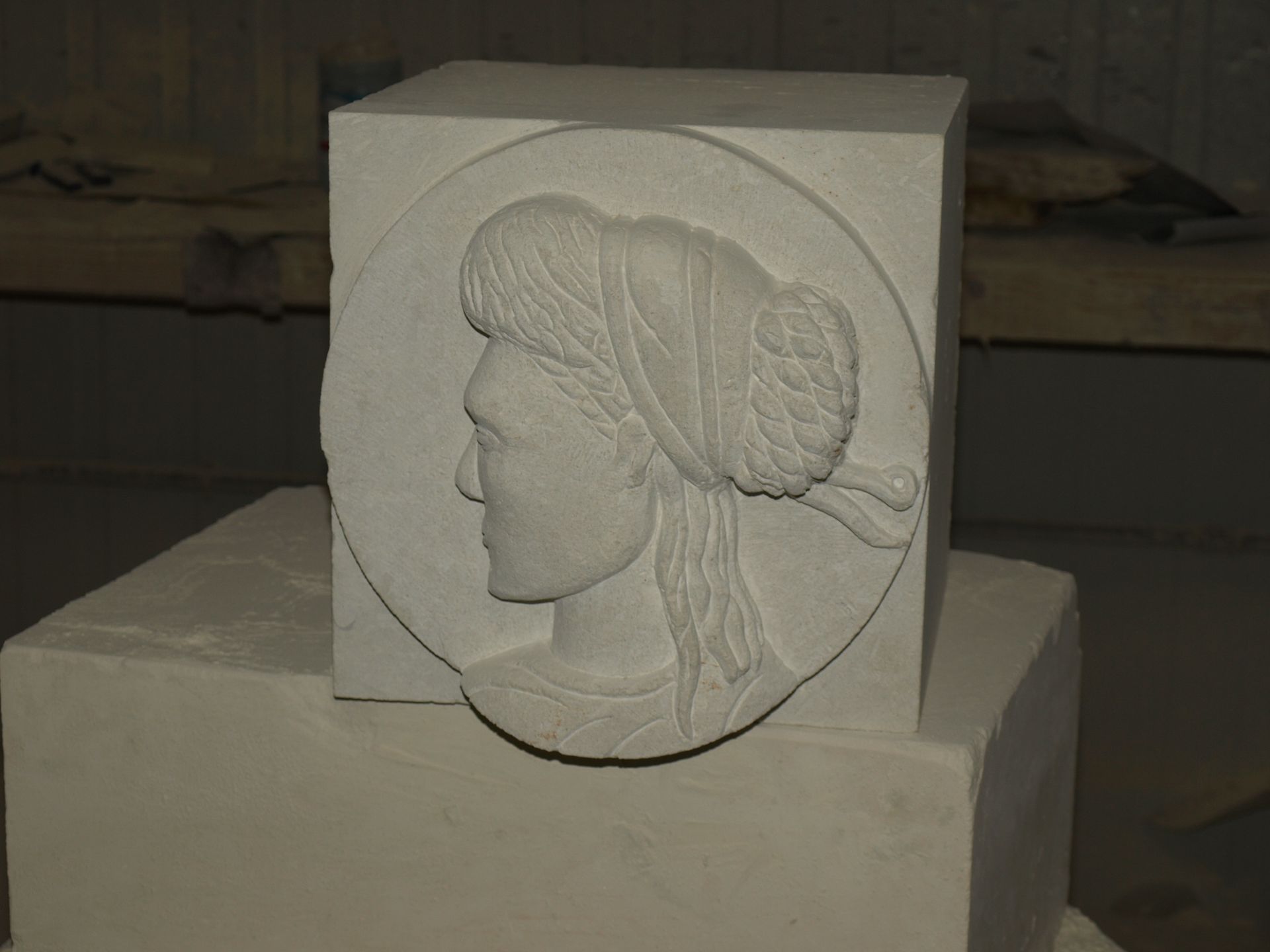 Un bas-relief en pierre représentant un portrait de profil dans un cadre circulaire, posé sur un bloc dans un atelier.