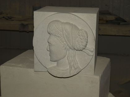 Un bas-relief en pierre représentant un portrait de profil dans un cadre circulaire, posé sur un bloc dans un atelier.