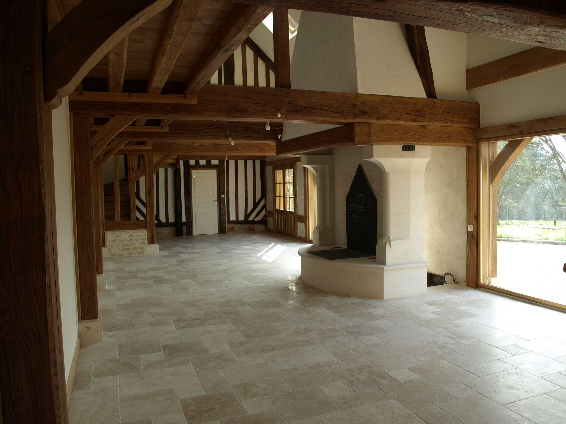 Une pièce spacieuse avec des poutres apparentes, une grande cheminée en pierre et un sol en carrelage clair, agrémentée de murs de style Tudor.