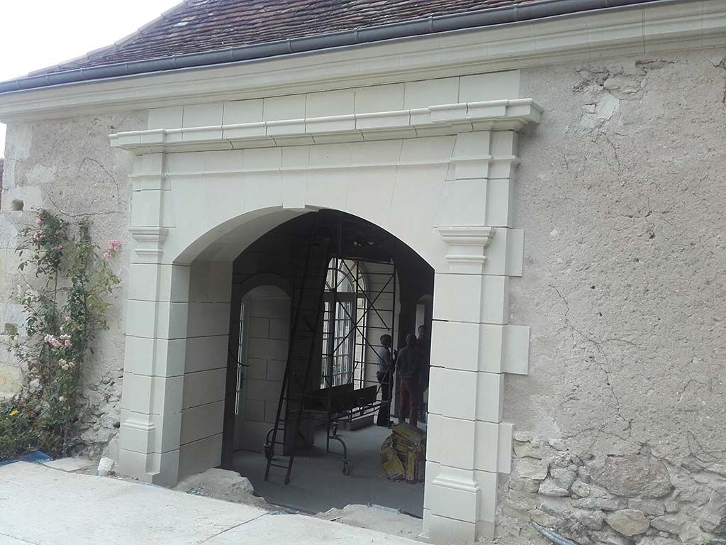 Une arche en pierre claire ornée encadre une entrée menant à une zone de construction avec des échafaudages.