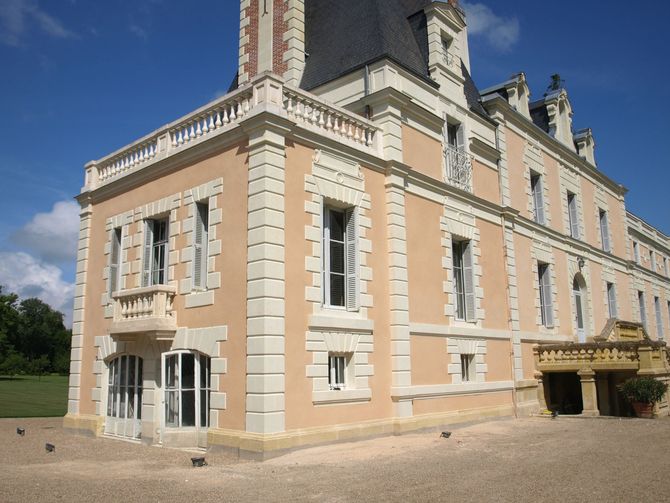 Un château français historique aux murs couleur pêche, aux chaînes d'angle en pierre et au toit d'ardoise, sous un ciel d'un bleu éclatant.