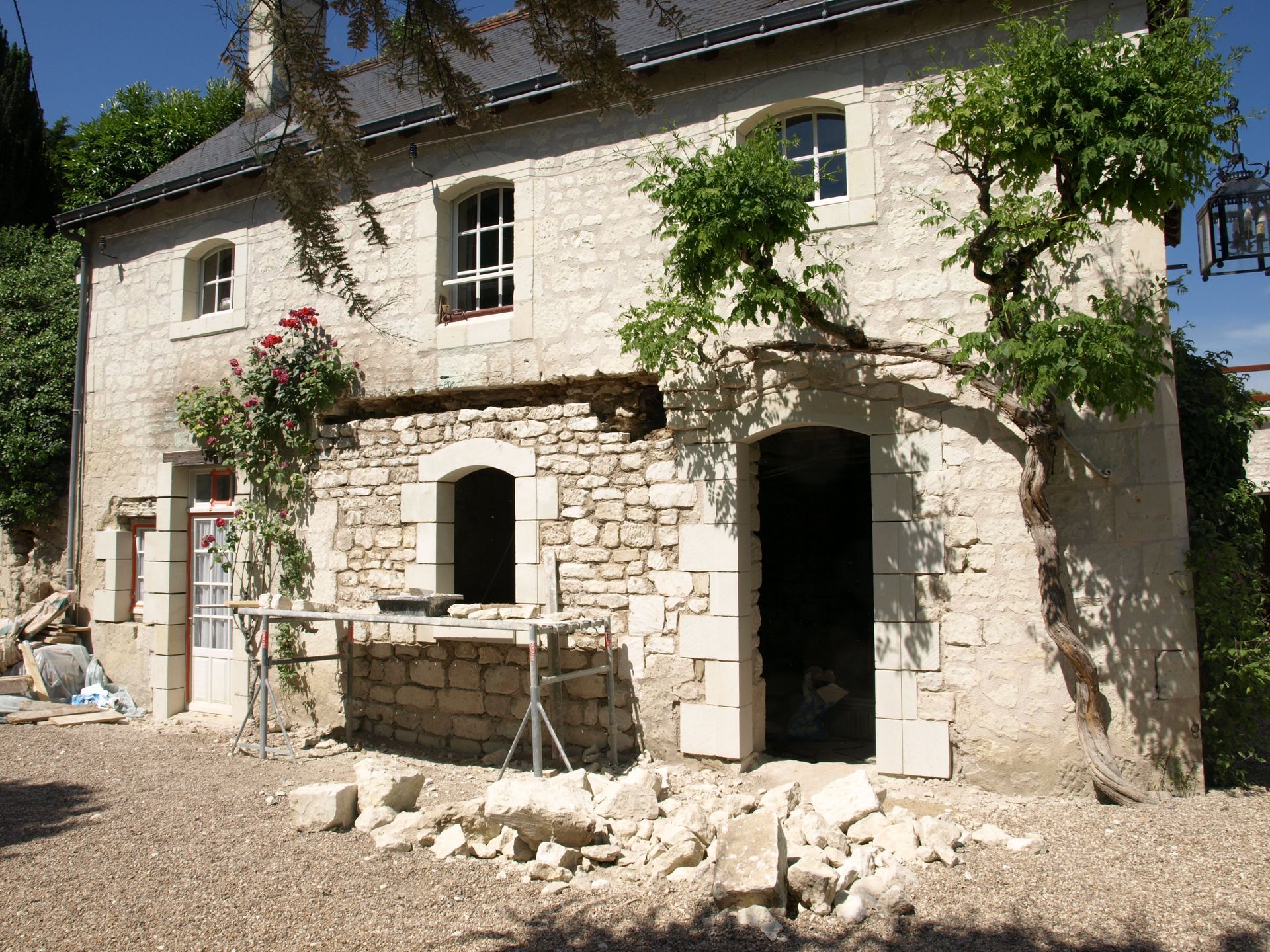 Une ferme en pierre en cours de rénovation, avec des échafaudages, des maçonneries apparentes et des tas de gravats dans la cour avant.