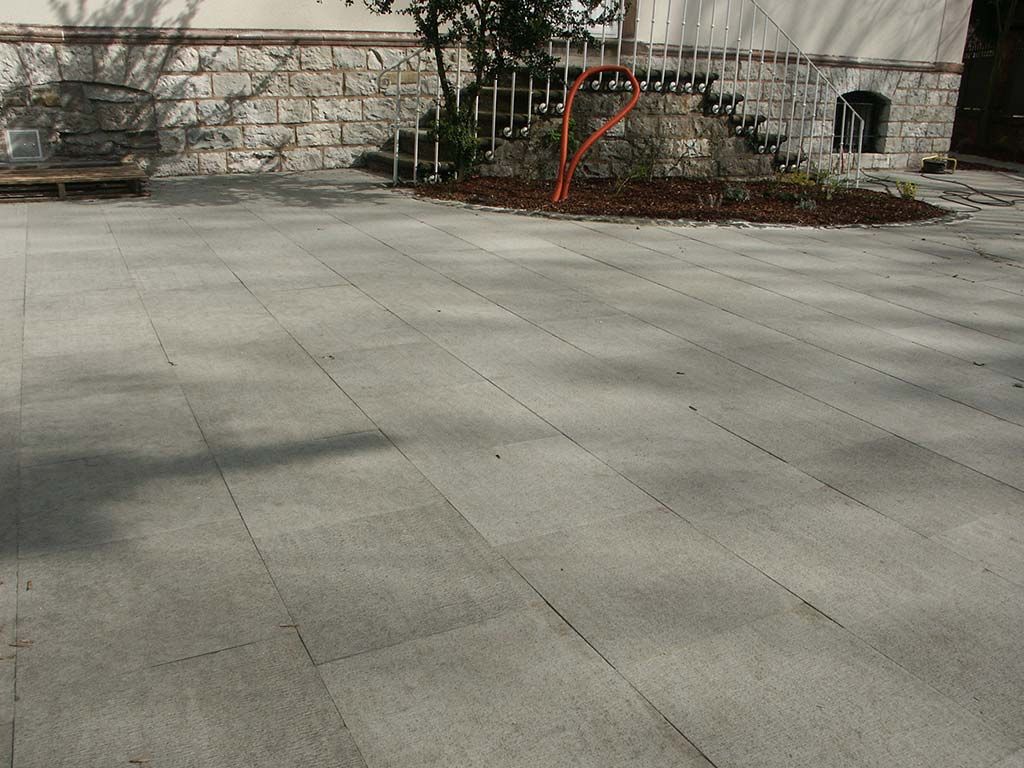 Une terrasse pavée aux lignes droites menant à un petit espace paysager et un mur d'enceinte en pierre en arrière-plan.