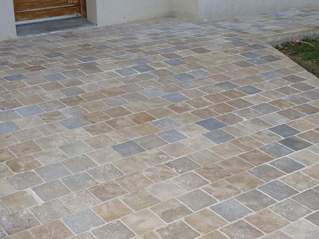 Une terrasse pavée de dalles rectangulaires en pierre de différentes nuances de brun, de gris et de beige, située devant la porte d'un bâtiment.