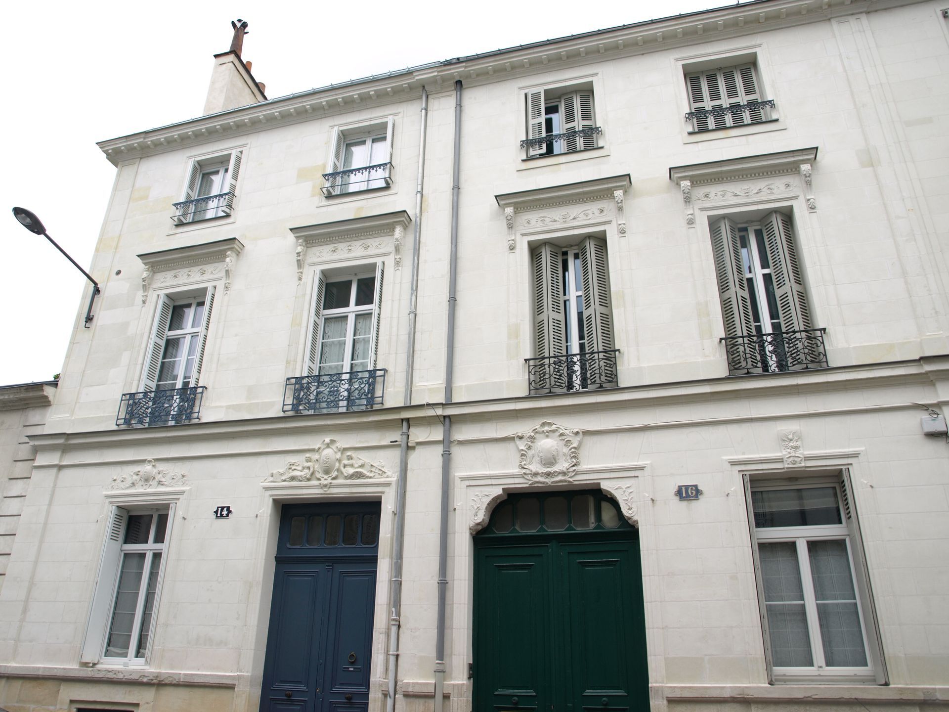 Un bâtiment de trois étages en pierre blanche avec deux grandes portes d'entrée, l'une bleu foncé et l'autre vert foncé, et des ornements en fer forgé.